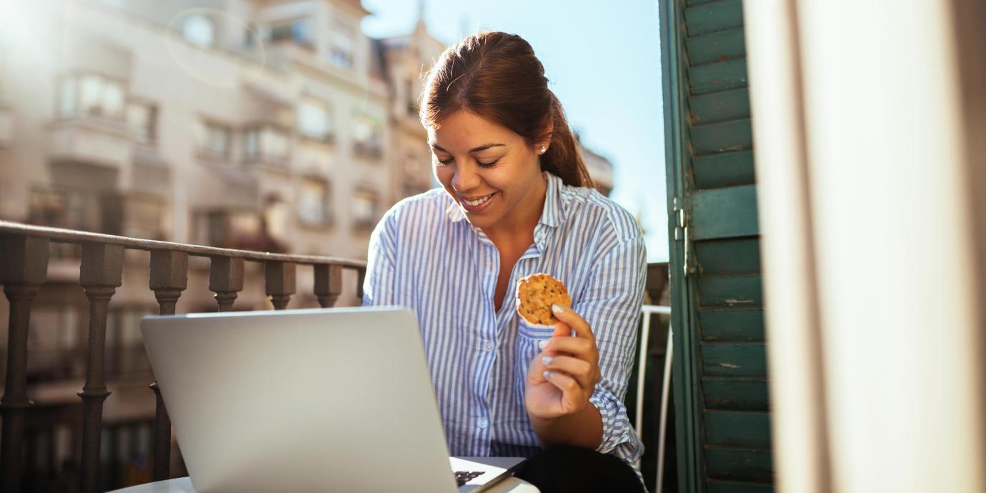 a businesswoman with a cookie in hand working happily on her laptop