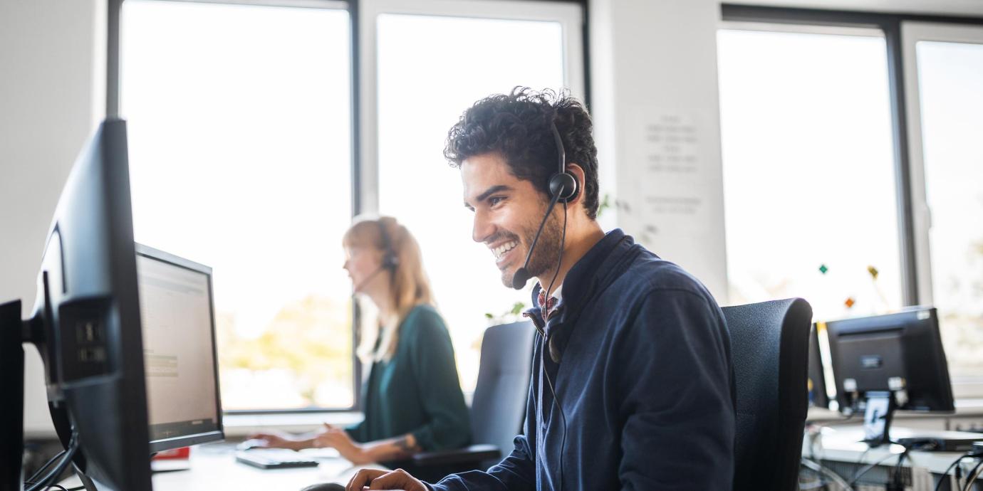 a smiling businessman with a headset on working on his computer advising customers